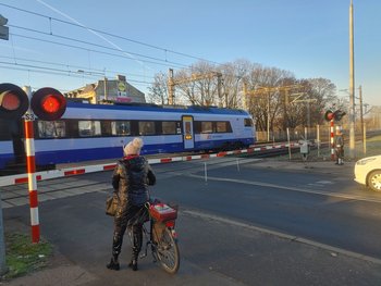 Rowerzystka przed zamkniętymi rogatkami przejazdu na Starołęce, obok sygnalizacja, w tle pociąg_fot.Radek Śledziński