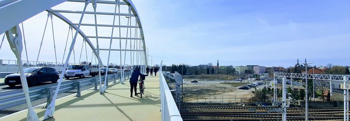 Piesi i rowerzyści idą po nowym wiadukcie w Łowiczu. Na jezdni sznur aut. W tle tory kolejowe i sieć trakcyjna. Fot. Anna Jadaś